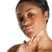 Une femme aux cheveux courts se touche délicatement le menton de la main droite, s'interrogeant sur son hyperpigmentation. Son expression est neutre, son regard légèrement hors champ sur un fond blanc. Dakar