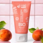 Un tube de MKL Crème mains certifiée BIO Abricot - 50ml est représenté sur un fond de carrelage rose, accompagné d'abricots frais et de feuilles vertes. Dakar