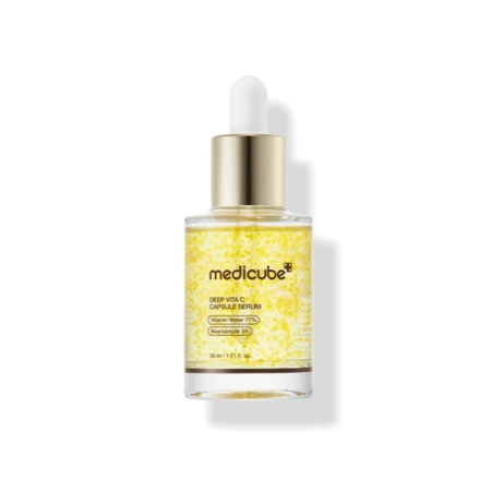 Medicube Deep Vita C Sérum Capsule Illuminateur Anti Tache 30 ml se présente dans un flacon compte-gouttes en verre avec un bouchon doré, un compte-gouttes blanc, et contient un liquide transparent avec des capsules jaunes. L'étiquette indique le nom du produit et les ingrédients. Dakar