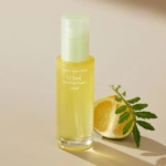 Un flacon de Goodal Green Tangerine Sérum Vitamine C Anti-Taches et Anti-imperfections 40 ml se tient debout à côté d'une mandarine verte coupée en tranches et d'une feuille sur une surface beige clair, doucement éclairée par la lumière naturelle. Dakar