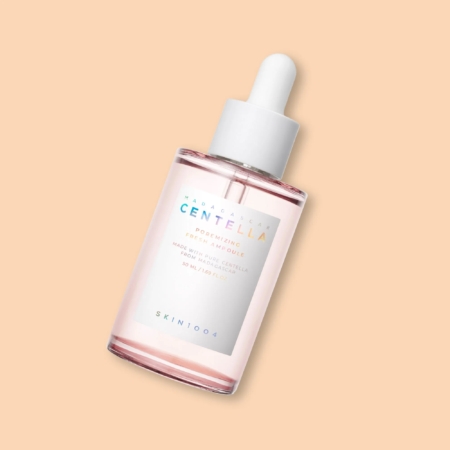 Un flacon compte-gouttes en verre étiqueté "SKIN1004 Madagascar Centella Ampoule Anti Pores Dilatés TOUS TYPES DE PEAU 50 ml" rempli d'un liquide rose transparent est présenté sur un fond beige. Dakar