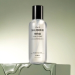Un flacon de Jumiso Mucine d'Escargot 95 % + Essence Peptide Anti Acné Peau Lisse 140 ml repose sur une surface réfléchissante, étiquetée « Mucine d'Escargot 95 % + Peptide ». Son liquide transparent contraste avec un dégradé vert clair, offrant une esthétique rafraîchissante. Dakar