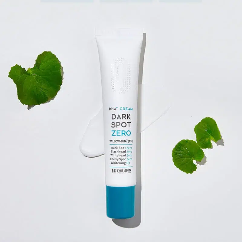 Un tube de Be The Skin Crème Multifonctions Éclaircissante et Anti Ride 35g repose sur une surface blanche, avec de la crème à côté et deux feuilles vertes à proximité. Le tube à bouchon bleu porte une étiquette blanche avec des informations sur le produit. Dakar