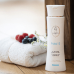 Bouteille blanche de Candés Gel Nettoyant Dermopurifiant 200 ml à côté d'une serviette pliée avec des baies et des fleurs sur une surface en bois
