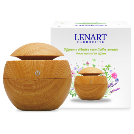 Un Diffuseur d'huiles Essentielles Nomade en bois, de forme sphérique et doté d'un bouton de mise en marche, est placé devant une boîte blanche "LENART HERBORISTE", avec des fleurs et l'image d'un diffuseur, ainsi que le parfum rafraîchissant de l'Eau Christian Lénart. Dakar