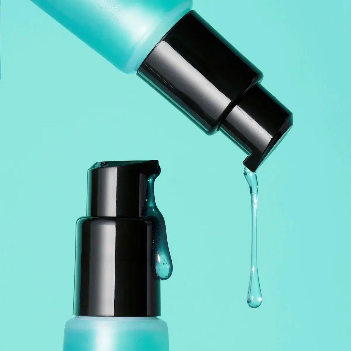 Gros plan de deux flacons-pompes bleus à bouchon noir d'Elf Base de Maquillage à Base de Gel Power Grip 24 ml sur un fond bleu. Un liquide transparent s'écoule des pompes supérieure et inférieure. Dakar