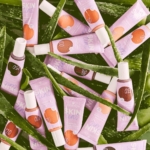 Une collection de tubes violets et blancs étiquetés « Essence Skin Tint Fond de Teint Teinté Hydratant SPF30 Finition Naturelle 30 ml » repose sur des feuilles d'aloe vera vertes. Ils présentent une gamme de nuances, mettant l'accent sur les soins de la peau et les ingrédients naturels, avec une présentation vibrante et captivante. Dakar