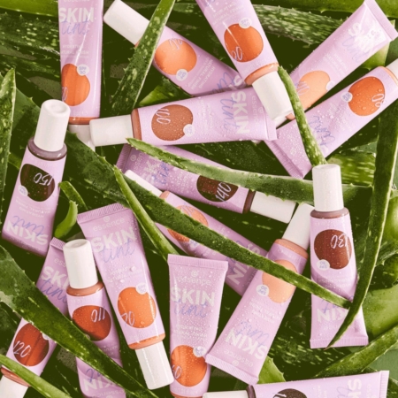 Une collection de tubes violets et blancs étiquetés « Essence Skin Tint Fond de Teint Teinté Hydratant SPF30 Finition Naturelle 30 ml » repose sur des feuilles d'aloe vera vertes. Ils présentent une gamme de nuances, mettant l'accent sur les soins de la peau et les ingrédients naturels, avec une présentation vibrante et captivante. Dakar