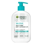 Un flacon blanc de Garnier Hautklar Salicylic Purifying Gentle Cleanser avec une pompe sarcelle est posé à côté de Essence Cosmetics Pretty Fast Nail Polish Blush Rush Vernis à Ongles 02 5 ml, avec des détails sur le produit en anglais, français et allemand. Dakar