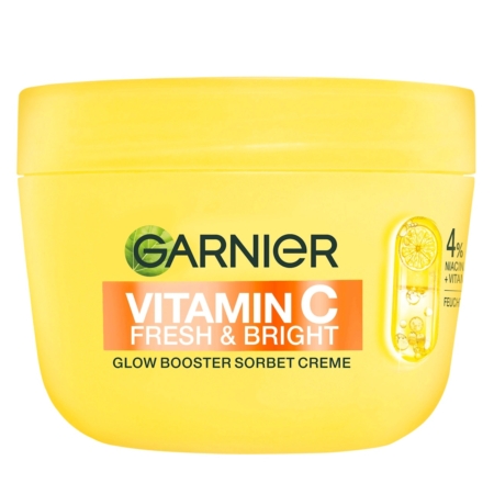 Un pot jaune de crème sorbet Garnier Vitamine C Fresh & Bright Glow Booster avec un graphique de tranches de citron et un texte sur la vitamine C se trouve à côté du brillant à lèvres Juicy Bomb Shiny Lipgloss 01 Proud Pitaya 10ml d'Essence Cosmetics, formant ainsi un duo de beauté radieux. Dakar