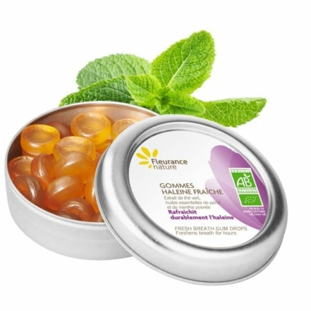 Une boîte de Gommes haleine fraîche Bio Complément alimentaire Fleurance Nature, avec son couvercle légèrement entrouverte, se dresse sur un fond inspiré de Dakar. Les gouttes ambrées scintillent aux côtés de feuilles de menthe fraîche, tandis que l'étiquette et le logo verts évoquent l'essence vivante du Sénégal. Dakar