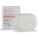 Une barre blanche de Ht26 Savon Visage Lumière Vitamine C Illuminateur 150g, estampillée "HT 26 Paris", se trouve devant sa boîte blanche étiquetée avec un texte orange et gris : "Ht26 Vitamine C Teint Lumière Glow-up Face Soap. Dakar