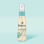 Un flacon de Biolane Spray d'huile d'amande douce 75ml avec une buse de pulvérisation sur fond bleu clair