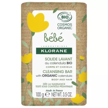 La barre rectangulaire de Klorane Bébé Savon Surgras Doux, étiquetée pour le corps et les cheveux, est présentée dans un emballage floral marron et jaune. La barre nettoyante certifiée biologique pèse 250 g (8.8 oz). Dakar