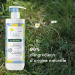 Un flacon de Klorane Lait Hydratant au Calendula 500 ml repose sur une herbe ornée de petites fleurs. Le texte indique « 96 % d'ingrédients d'origine naturelle. Dakar