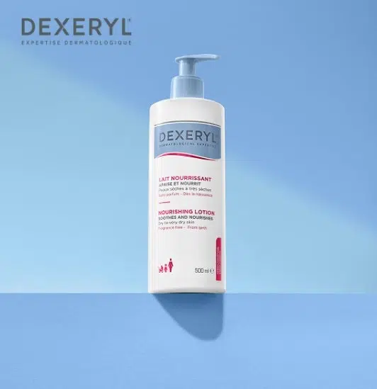 Un flacon de 500 ml de Dexeryl Essentiel Lait Riche Nourrissant avec une pompe bleue repose sur une surface bleue. Son étiquette, en français et en anglais, indique le nom du produit et son volume. Dakar