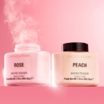 Deux pots de Poudre de Finition Libre Bake and Finish de MakeUp Revolution, étiquetés « Rose » et « Peach », contiennent chacun 32 g. Sur un fond rose, le pot « Rose » libère une goutte dans l'air tandis que le pot « Peach » reste stable. Dakar
