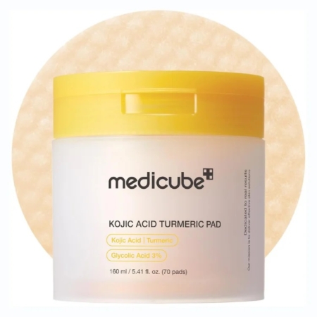 Un contenant rond blanc et jaune de medicube - Kojic Acid Turmeric Pad - Disques toniques éclat anti-taches est présenté devant un tampon beige texturé, l'étiquette mettant en évidence l'acide kojique, le curcuma et l'acide glycolique 3 % parmi ses ingrédients. Dakar