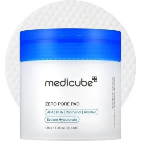 Un récipient blanc avec un couvercle bleu étiqueté "Medicube Zero Pore Pad 2.0 Tampons Exfoliant Anti Pore Dilate et Acné 70 pads" se trouve devant un tampon rond texturé, mettant en évidence l'AHA, le BHA, le Panthénol, l'Allantoïne et l'Hyaluronate de sodium. Dakar