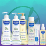 Cinq produits Mustela Ma Première Gamme Bébé, ainsi qu'une éponge de bain et un sac de naissance gratuit, sont présentés sur un fond bleu-vert aux subtils motifs de feuilles. Dakar