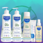 Six produits Mustela Les Essentiels Pour la Valise de Maternité, ainsi qu'une éponge de bain et un doudou gratuits, sont présentés sur un fond abstrait bleu et sarcelle. Dakar