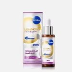 Un flacon de 30 ml de Nivea Luminous Skin Glow Sérum Éclat Immédiat avec compte-gouttes se trouve à côté de sa boîte blanche et violette, avec des accents dorés et un texte en français présentant la marque et les informations sur le produit. Dakar