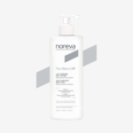 Un flacon blanc de Noreva Trio White XP lait corporel anti-taches 400 ml avec pompe sur fond gris clair