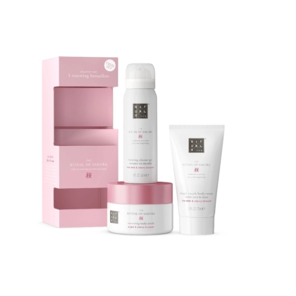 Un coffret cadeau pour femme Rituals The Ritual Of Sakura rose et blanc avec gel douche moussant, gommage corporel et crème pour le corps est présenté à côté d'une boîte ouverte sur le thème des fleurs de cerisier roses. Dakar