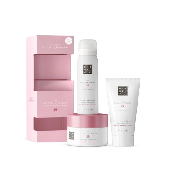 Un coffret cadeau pour femme Rituals The Ritual Of Sakura rose et blanc avec gel douche moussant, gommage corporel et crème pour le corps est présenté à côté d'une boîte ouverte sur le thème des fleurs de cerisier roses. Dakar