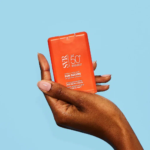 Main tenant un flacon de crème solaire rouge SVR SUN SECURE Spray Solaire Pocket Hydratant Invisible SPF50+ Peaux Hypersensibles au Soleil 20 ml sur fond bleu clair. dakar