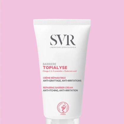 Un tube blanc de SVR Topialyse Barrière Crème Réparatrices Apaisante Anti Grattage Et Rougeur 50 ml avec un texte noir et rose se tient debout sur un fond rose clair uni. Dakar