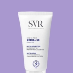 Un tube blanc de Svr Xerial 30 Crème Pieds Nutri-Réparateur 50 ml est présenté sur un fond violet clair, avec des textes en français et en anglais soulignant ses bienfaits hydratants, préventifs des callosités et réparateurs. Dakar
