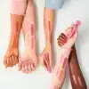 Trois bras de différentes teintes de peau présentent des échantillons de Blush Liquide Baby Got Blush d'Essence Cosmetics dans des tons rose et pêche sur fond blanc. Chaque bras tient un tube de blush, avec les échantillons étiquetés 10, 20, 30 et 40. Dakar