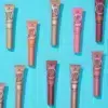 Une mise à plat de tubes de maquillage Essence sur un fond bleu vif. Les tubes sont disposés selon un motif en forme de grille et comprennent des nuances des gammes « Baby Got Blush » et « Baby Got Glow » dans diverses couleurs rose, corail et nude. Dakar
