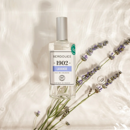 Un flacon d'Eau de Cologne BERDOUES Lavande 125 ml flotte sur l'eau ondulante parmi les brins de lavande, avec son design clair, son bouchon argenté et son étiquette minimaliste. Dakar