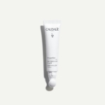 Un tube blanc de CAUDALIE Vinoperfect Soin Éclaircissant Regard 15 ml est placé verticalement sur un fond gris clair, affichant le nom et la marque du produit sur le devant. Dakar