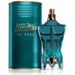 Un flacon de parfum turquoise, en forme de torse masculin et orné d'une touche de feuille d'or, se dresse devant un récipient cylindrique assorti. L'étiquette indique « Jean Paul Gaultier Le Beau 75 ml. Dakar