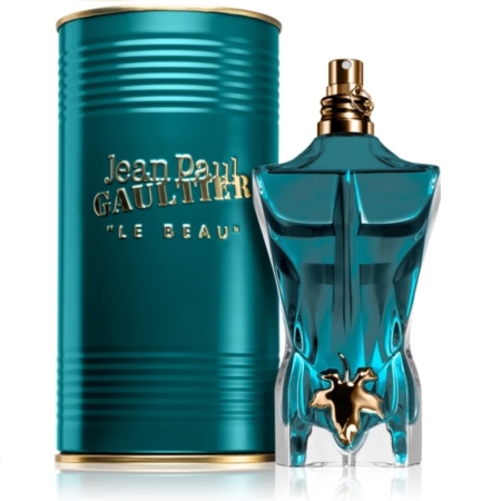 Un flacon de parfum turquoise, en forme de torse masculin et orné d'une touche de feuille d'or, se dresse devant un récipient cylindrique assorti. L'étiquette indique « Jean Paul Gaultier Le Beau 75 ml. Dakar