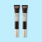 Deux tubes identiques marron foncé de SKIN1004 Madagascar Centella Probio Cica Bakuchiol Crème Yeux Anti Rides Effets Apaisants 20 ml avec des bouchons beiges, debout sur un fond bleu clair. Dakar
