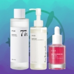 Le fond bleu sarcelle présente trois produits de soin de la peau Anua : le tonique apaisant Heartleaf dans un flacon transparent, l'huile nettoyante Heartleaf Pore Control avec une pompe et le sérum correcteur de taches brunes Niacinamide 10 % + TXA 4 % dans un flacon compte-gouttes. Dakar