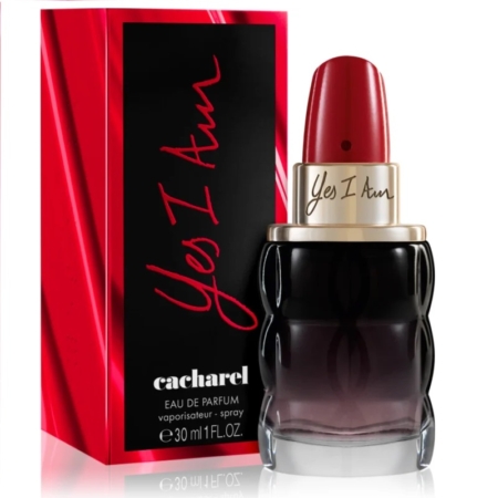 Un flacon de parfum Cacharel Yes I Am 30 ml, conçu comme un rouge à lèvres avec un bouchon rouge et une base sombre, est posé à côté d'un coffret rouge et noir assorti. Tous deux arborent en évidence « Yes I Am » et « Cacharel » en dessous, dégageant une élégance proche de celle de l'Eau de Parfum La Rive Poétique. Dakar