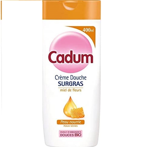 Un flacon de Cadum Crème Douche, 400 ml, avec un bouchon rose et orange. L'étiquette présente « miel de fleurs », une image de nid d'abeille, et mentionne « peau nourrie », « huille d'amandes » et « douces bio ». Dakar