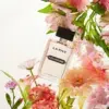 Un flacon de parfum étiqueté « La Rive Charisme » est entouré de fleurs roses et pêche vibrantes avec un feuillage vert, sur fond blanc. Dakar