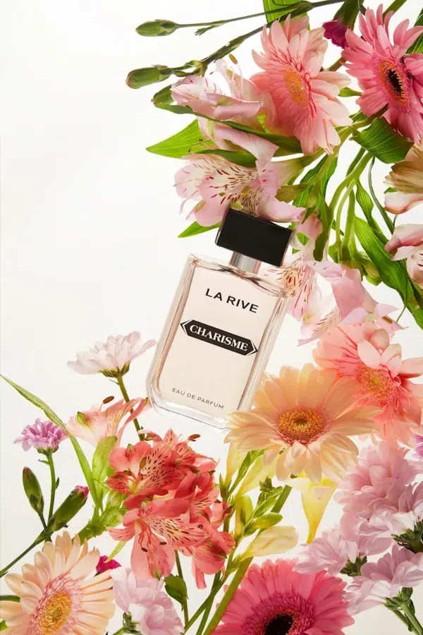 Un flacon de parfum étiqueté « La Rive Charisme » est entouré de fleurs roses et pêche vibrantes avec un feuillage vert, sur fond blanc. Dakar