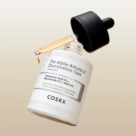 Un flacon de 30 ml de Cosrx The Alpha-Arbutin 2 Sérum Anti Taches et Unifiant avec compte-gouttes distribue du liquide. Des ingrédients comme l'acide tranexamique et la niacinamide sont mis en valeur sur l'étiquette. Le flacon est élégamment incliné sur un fond neutre et clair. Dakar