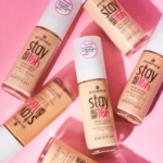 Les flacons d'Essence Fond de Teint 16H Longue Tenue en 50 Soft Caramel sont élégamment disposés sur un fond rose. Les flacons, droits ou inclinés, affichent leurs étiquettes, l'un d'eux affichant un autocollant déclarant qu'il ne contient ni silicones, ni parabènes, ni huiles minérales. Dakar