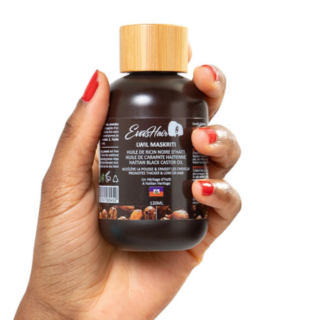 Une main avec du vernis à ongles rouge tient une bouteille marron foncé de 120 ml étiquetée « Evashair huile de ricin », mettant en valeur l'huile de ricin noire haïtienne de première qualité enrichie en carapate et menthe poivrée. Le fond est blanc éclatant, parfait pour In HairCare. Dakar