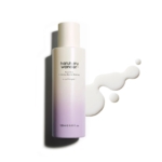 L'essence barrière hydratante et crémeuse riche Haruharu Wonder Black Rice Probiotics 120 ml de KSECRET SÉOUL 1988 se présente dans un flacon cylindrique au dégradé allant du blanc au violet clair, debout tandis que le liquide se déverse astucieusement à côté. Dakar