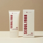 Un tube de KSECRET SÉOUL 1988 Essence Réparatrice Mucine d'Escargot se dresse à côté de son coffret, tous deux blanc cassé avec un texte rouge audacieux, évoquant l'élégance avec son motif mucine d'escargot sous un éclairage doux sur fond neutre. Dakar