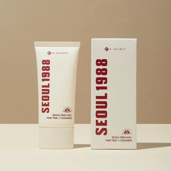 Un tube de KSECRET SÉOUL 1988 Essence Réparatrice Mucine d'Escargot se dresse à côté de son coffret, tous deux blanc cassé avec un texte rouge audacieux, évoquant l'élégance avec son motif mucine d'escargot sous un éclairage doux sur fond neutre. Dakar